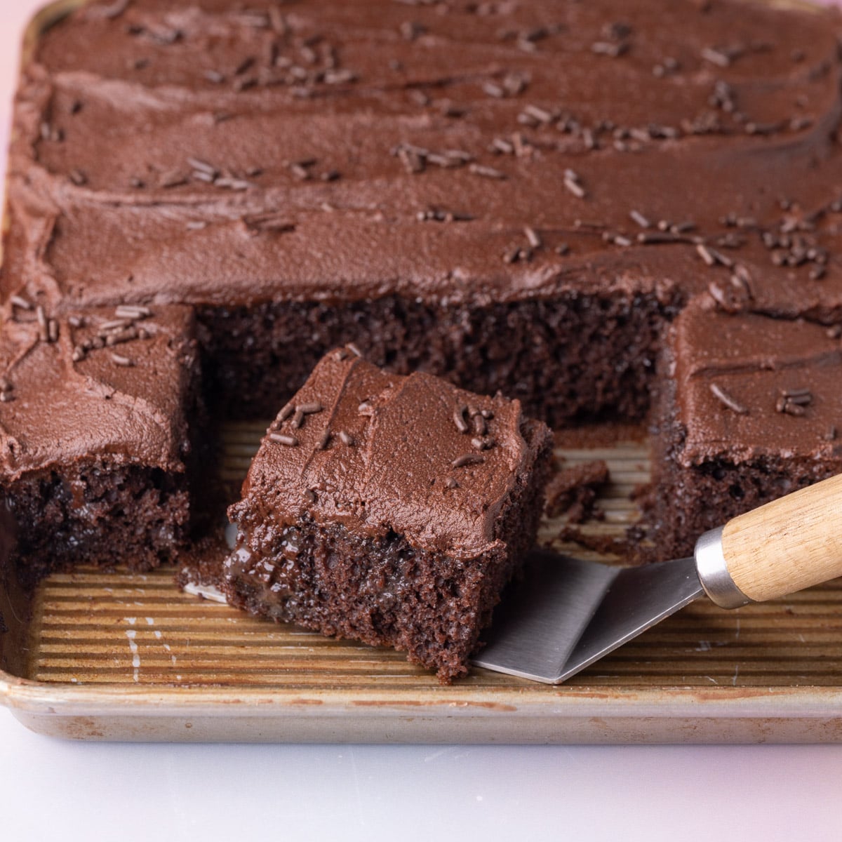 Taking a serving of chocolate poke cake off of the baking pan, showing the super-moist texture on the inside.