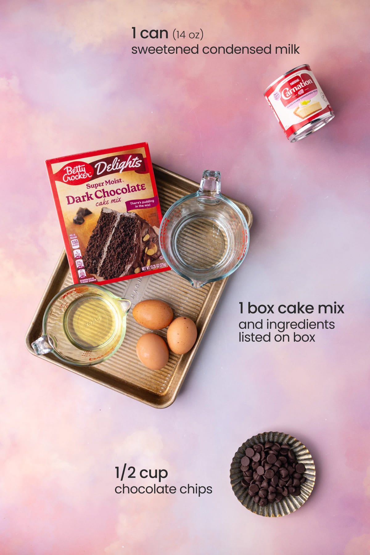 Overhead view of the ingredients needed for chocolate poke cake - condensed milk, box cake mix on a tray with eggs, water and oil, and chocolate chips.