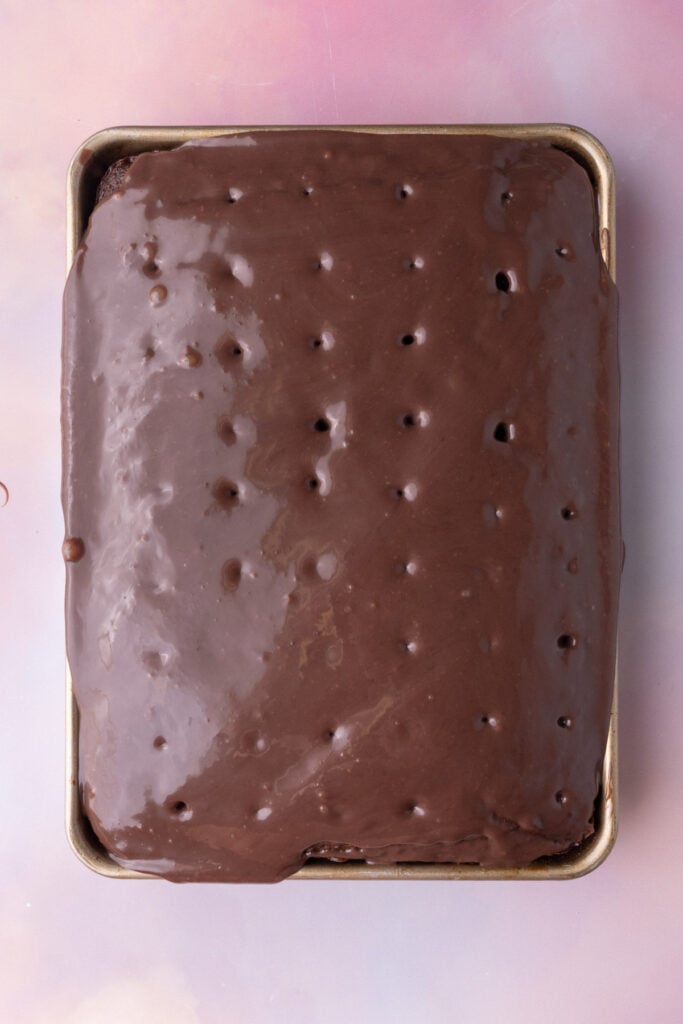 Chocolate and condensed milk mixture sinking into holes poked in a chocolate cake.