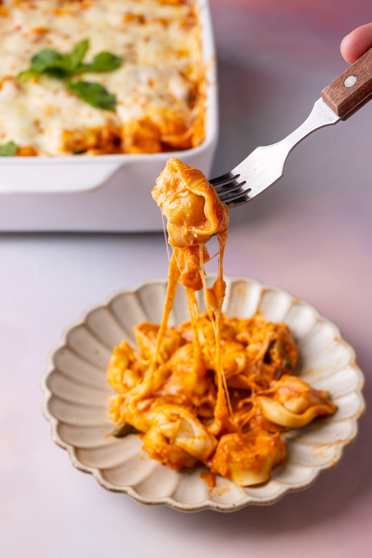 Grabbing a forkful of cheese tortellini casserole from a serving on a plate.