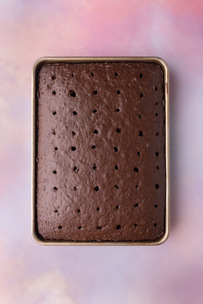 Chocolate cake fresh out of the oven with holes poked into the top with a straw.