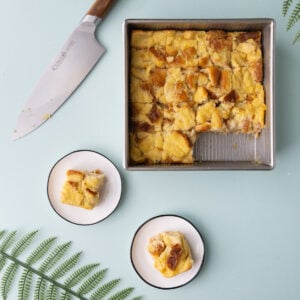 Bread pudding with crushed pineapple on a blue background with tropical leaves.