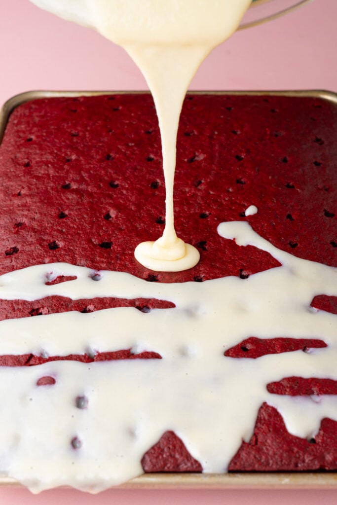 Pouring cream cheese condensed milk mixture over red velvet poke cake.