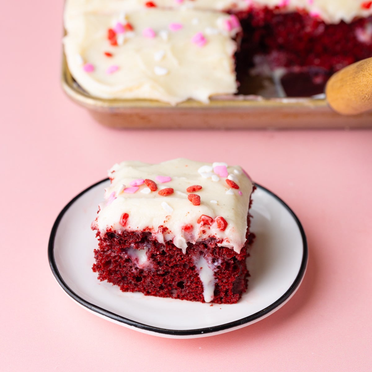 Slice of red velvet poke cake with sweetened condensed milk sunk into the holes, showing in spots on the cake.