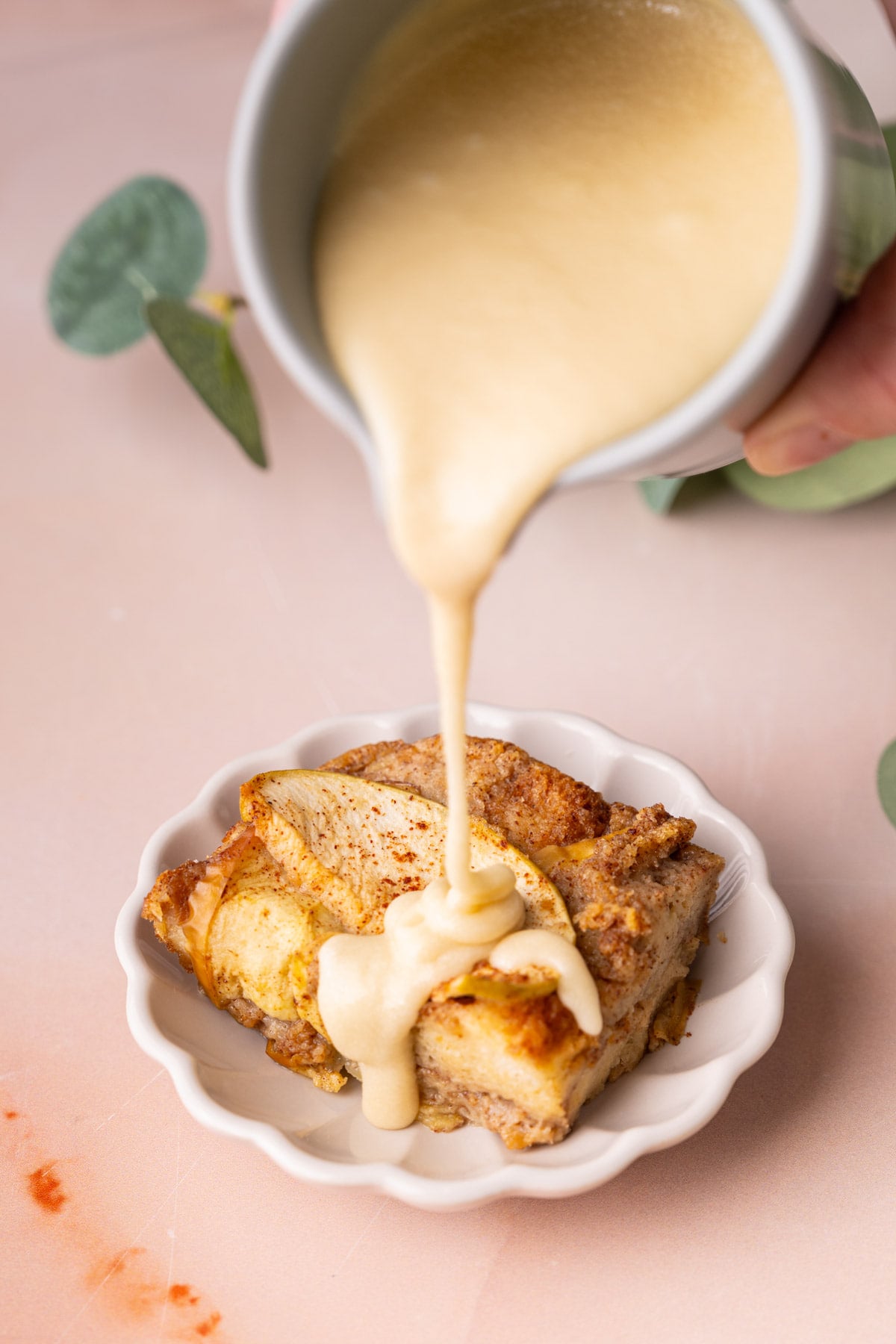Pouring fresh maple glaze over a slice of apple bread pudding to add extra flavor and moisture.