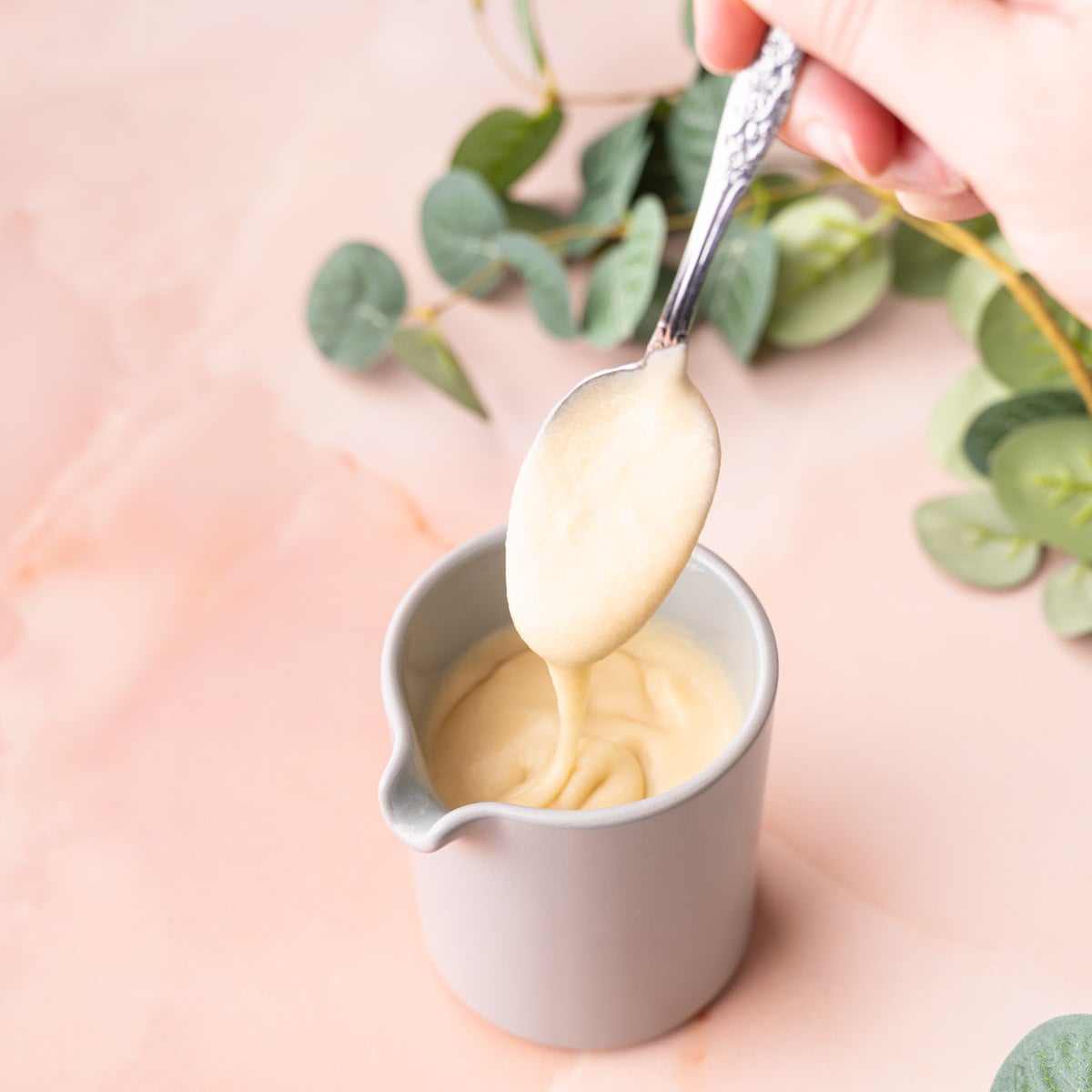 Maple icing made with just 4 ingredients drizzling off of a spoon and into a creamer.