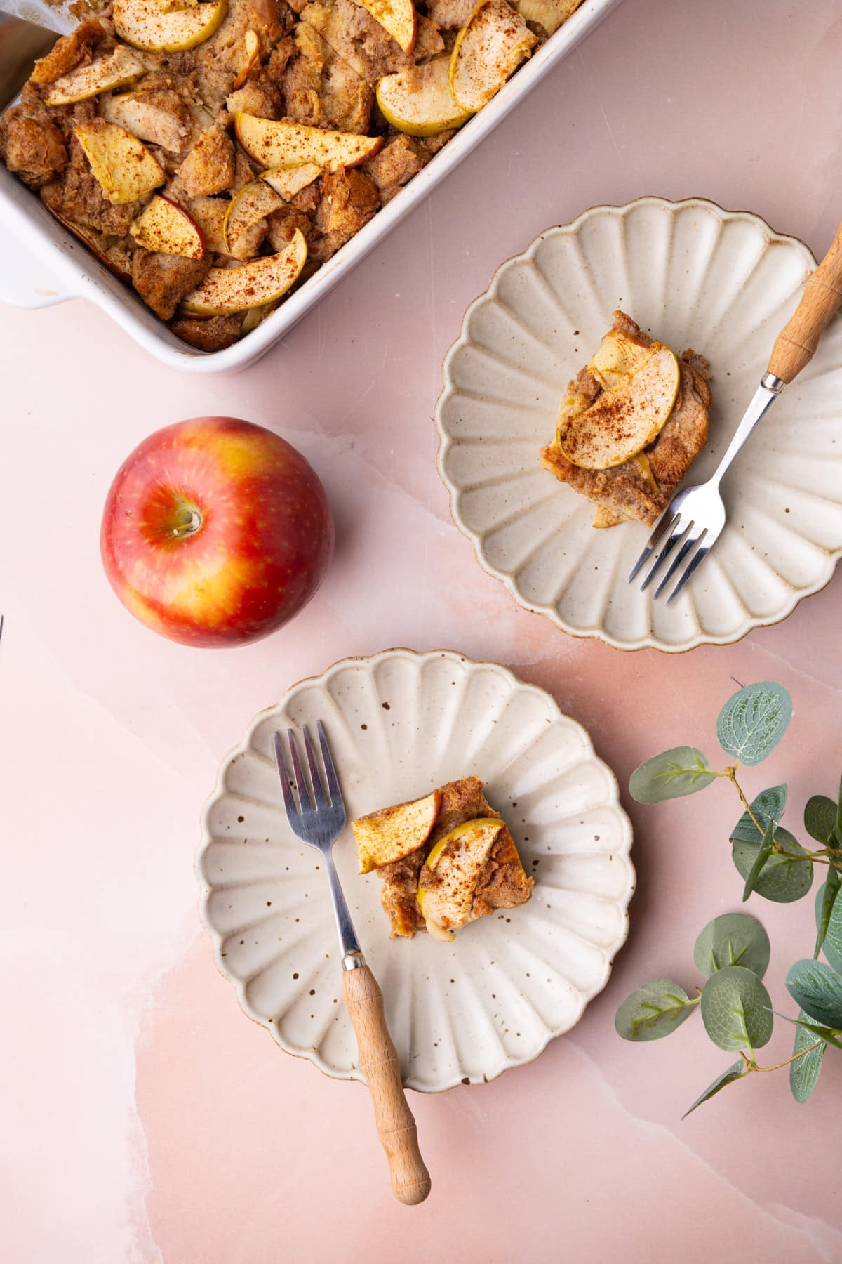 Two scalloped edge plates with slices of warm apple bread pudding on them.