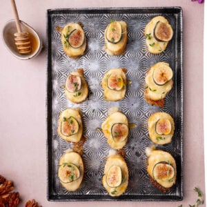 Brie Fig Crostini with fresh thyme and honey on a hammered metal tray served with extra honey and a honey dipper.