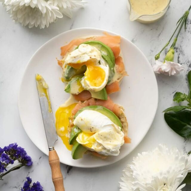 This Smoked Salmon Eggs Benedict features a zesty Hollandaise sauce poured over a perfectly poached egg and stacked atop creamy avocado, smoked salmon, and a warm toasted English Muffin.

Hollandaise Sauce
-4 tablespoons unsalted butter
-2 large egg yolks
-1 tablespoon grainy mustard
-1 tablespoon lemon juice
-¼ teaspoon salt
-¼ teaspoon black pepper
-1 pinch of cayenne pepper

-Separate your egg yolks from the whites by cracking the eggshell in half over a small bowl.
-Transfer the egg yolk back and forth between the two halves of eggshell, allowing the egg white to fall into the bowl underneath. Then, place the yolk in a small bowl and repeat with the second egg.
-In a microwave-safe dish, melt the butter in 20-second intervals until it is completely liquefied.
Add the yolks, mustard, lemon juice, salt, and pepper to your blender. Turn the blender on high. With the blender on, slowly pour in the hot butter and blend for another 10-15 seconds until smooth.

Poached Eggs
-12 cups boiling water
-½ cup white distilled vinegar (or apple cider vinegar)
-4 large eggs

-In a large pot, bring 12 cups of water and 1/2 cup of white distilled vinegar to a rolling boil.
-Crack your egg into a small ramekin or bowl. This will give you a chance to remove any eggshells that may have fallen in. It also allows you to drop the egg into the water bath more easily.
-Stir the boiling water vigorously to form a whirlpool in the center of your pot. Drop the egg in the center of your whirlpool and cook for 3 minutes. Remove carefully and set aside to dry. Repeat for all 4 eggs, cooking for 3 minutes each time.

Eggs Benedict
-2 English Muffins
-3 ounces smoked salmon
-1 avocado
-salt and pepper to taste

-Prep your ingredients by toasting your English Muffins, slicing and seasoning your avocado with salt and pepper, and separating 4 English-muffin-sized portions of smoked salmon.
-Add an even layer of smoked salmon on each piece of English Muffin and top with sliced and seasoned avocado.
-Top with poached eggs and pour over a generous amount of Hollandaise sauce. Serve warm.